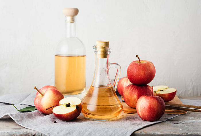 Jar of apple cider vinegar surrounded by apples on a tea towel.