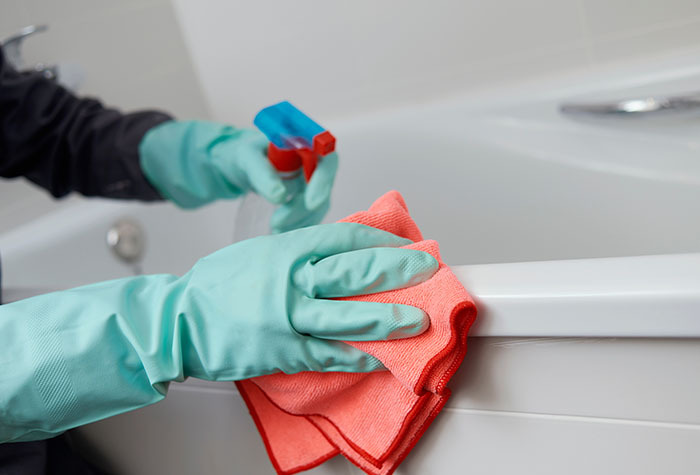 Person cleaning a bathtub with cleaning spray and a cloth.