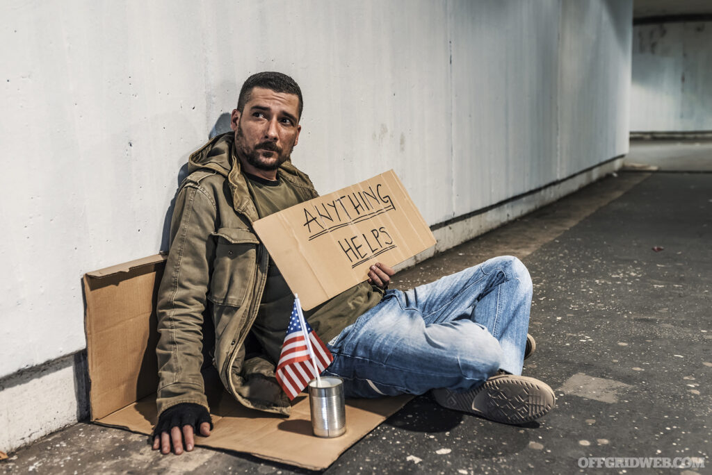 Photo of a pan handler sitting on the ground with a cardboard sign and a small American flag sitting in an unlabeled tin can.