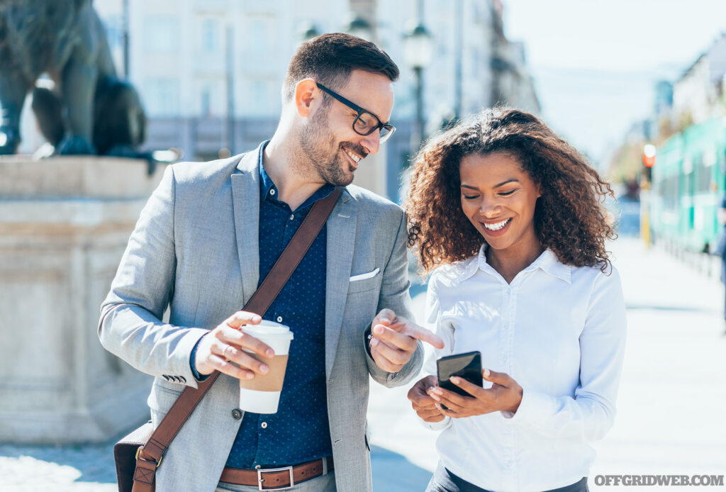 Photo of an adult male and adult female walking down the sidewalk smiling and looking at the same phone screen.