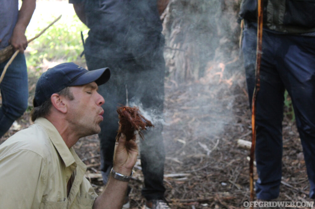 The instructor for Coyne Survival School Survival Skills Certification blows on an ember started with a bow drill.