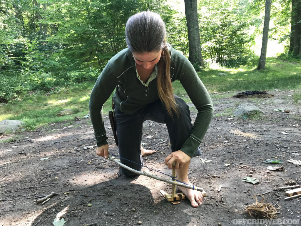 Photo of Carleigh Starting a fire with the bow drill method.