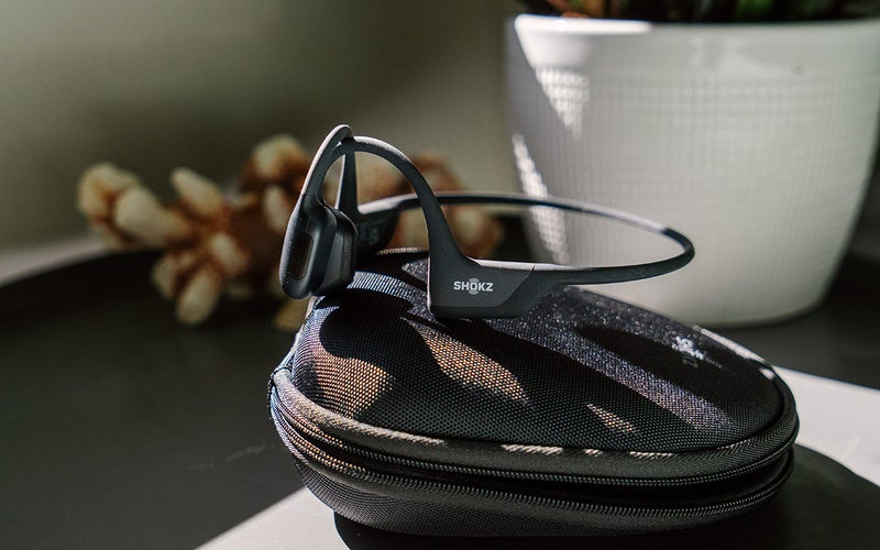 A pair of Shokz OpenRun Pro bone-conduction headphones rest on their case on an end table.