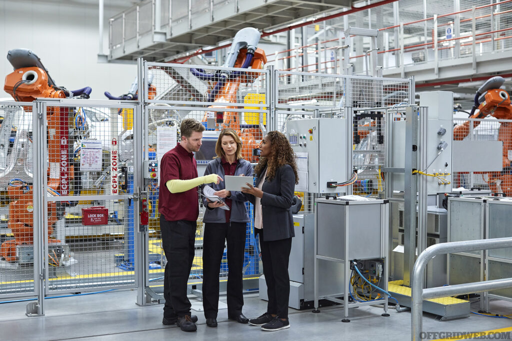 Full length of engineers discussing in car plant. Male and female workers are with digital tablet. Professionals are standing in automobile industry.