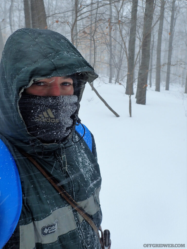 Photo of a man standing in a snowy forest with a snow crusted scarf across his face.
