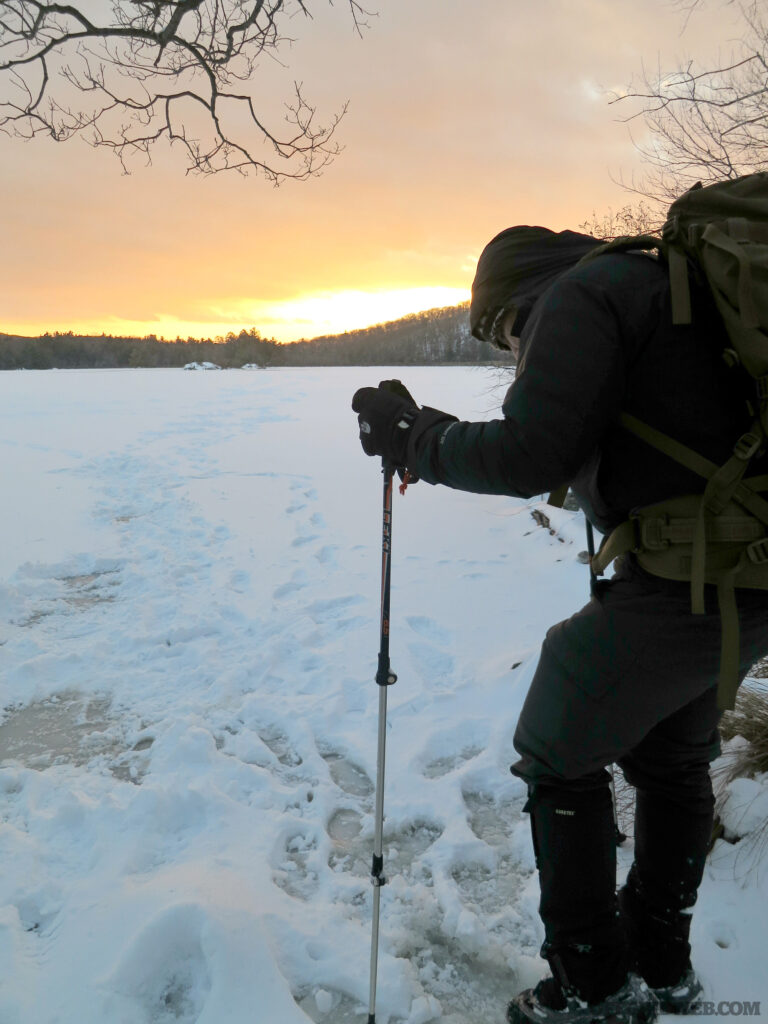Photo of a winter hiker standing next to a field as the sun sets.