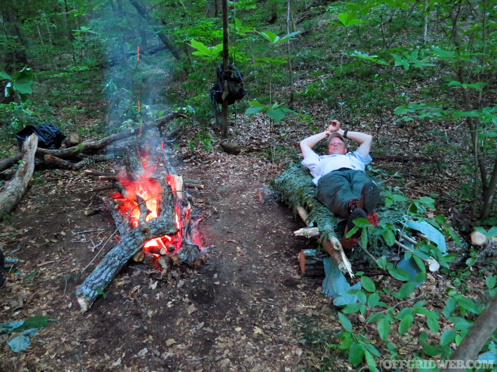 A man sleeping next to a fire on the forest floor.