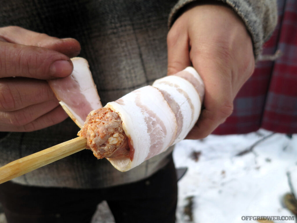 Photo of camp food on a stick being wrapped in bacon.