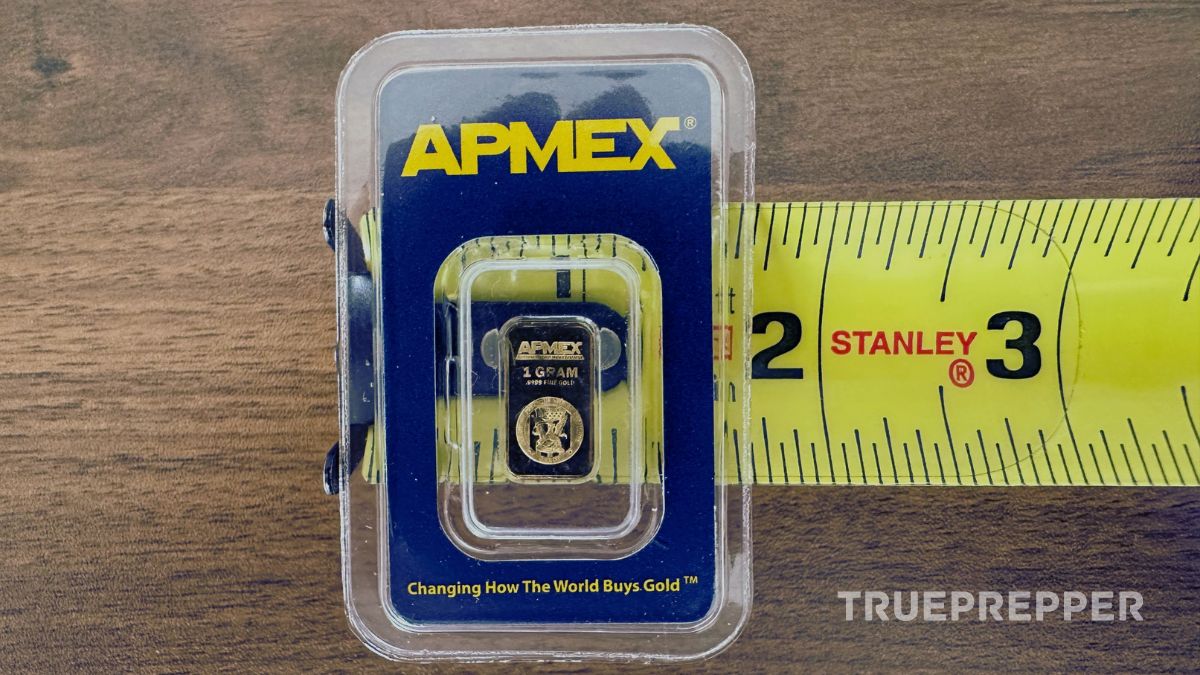 One gram gold bar in assay sitting on top of tape measure showing small size.