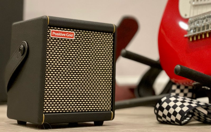 Positive Grid Spark Mini practice amp Bluetooth speaker on the floor next to a red guitar