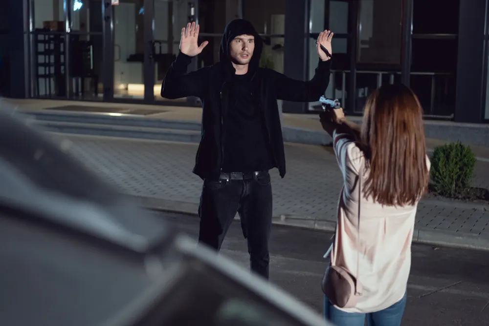 A girl pointing a gun to an assailant.